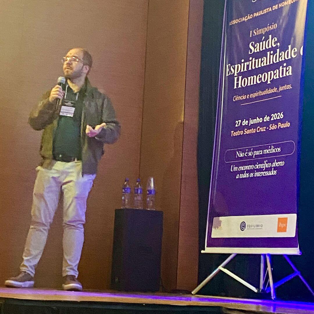 Dr. Everton de Oliveira Maraldi falando ao microfone no palco do simpósio, ao lado do banner da APH.